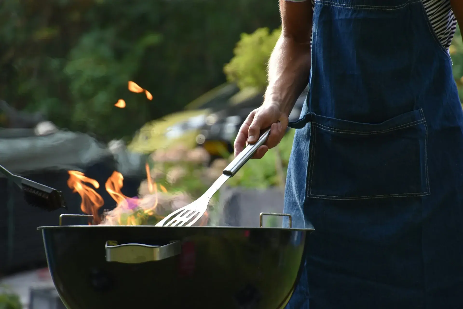 Person i förkläde som grillar över ett grillgaller med lågor under